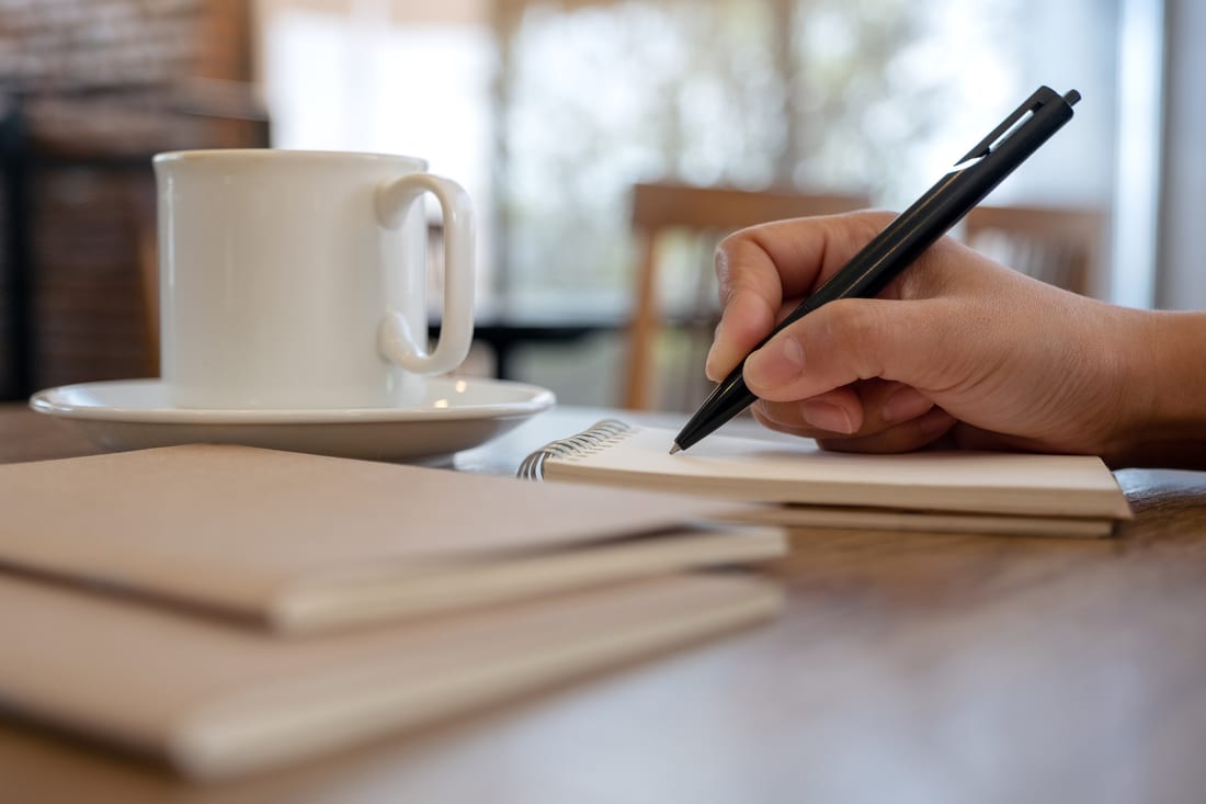 Hand writing notes with a pen next to a cup of coffee